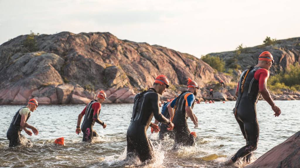 Athletes entering open water during a slow-paced swimrun race with rocky shoreline in the background